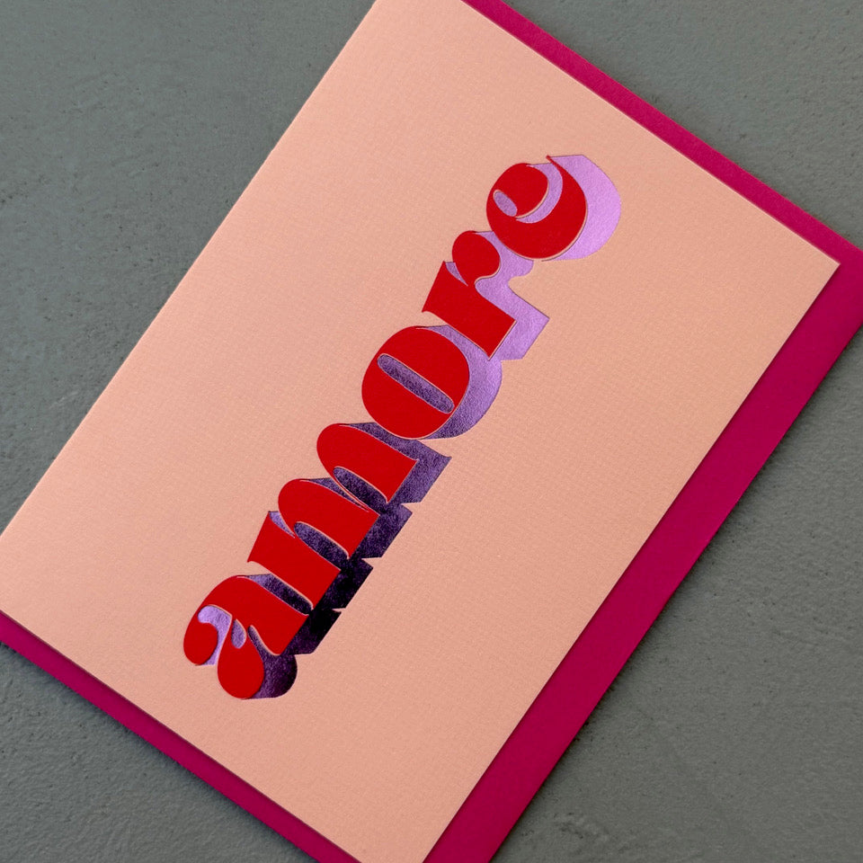 Angled view of the peach Amore card showing the red lettering and reflective purple foil.
