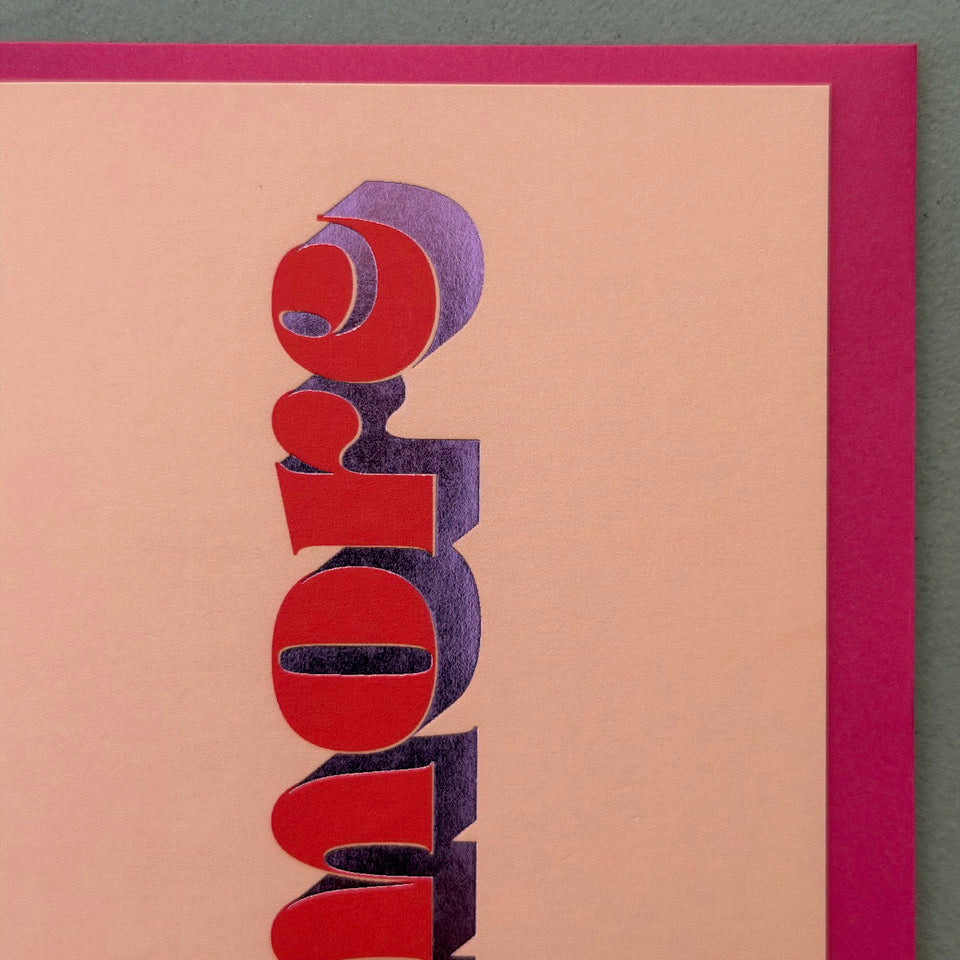Close-up of the red lettering and metallic purple foil detail on the peach Amore card.