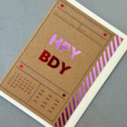 Angled view of the Birthday Ticket greeting card with a cream envelope, showcasing the modern ticket design and colourful foil accents.