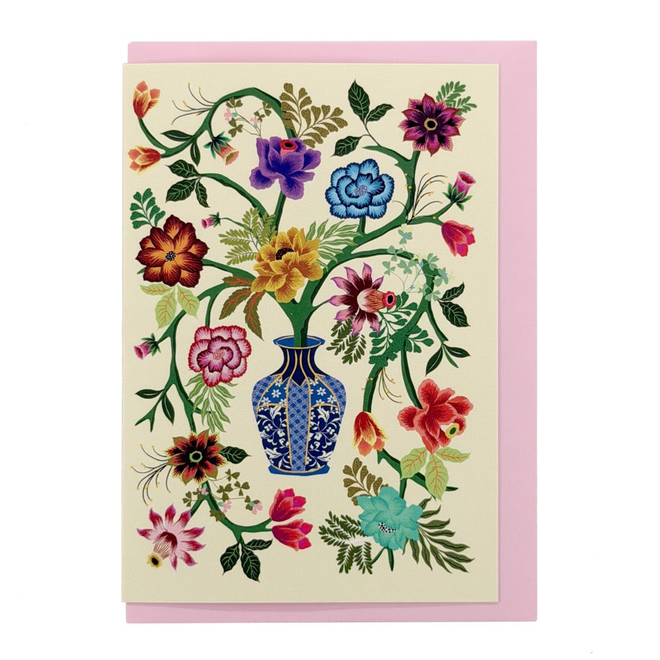 Illustrated floral greeting card featuring a decorative blue vase filled with colourful flowers and trailing green stems, paired with a soft pink envelope.
