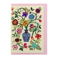 Illustrated floral greeting card featuring a decorative blue vase filled with colourful flowers and trailing green stems, paired with a soft pink envelope.