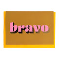 Ochre Bravo card with pink lettering and gold foil detail, shown with a mustard yellow envelope.