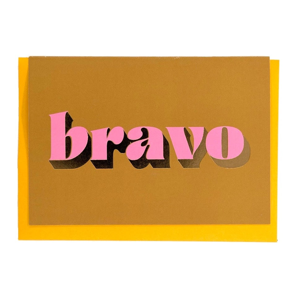 Ochre Bravo card with pink lettering and gold foil detail, shown with a mustard yellow envelope.