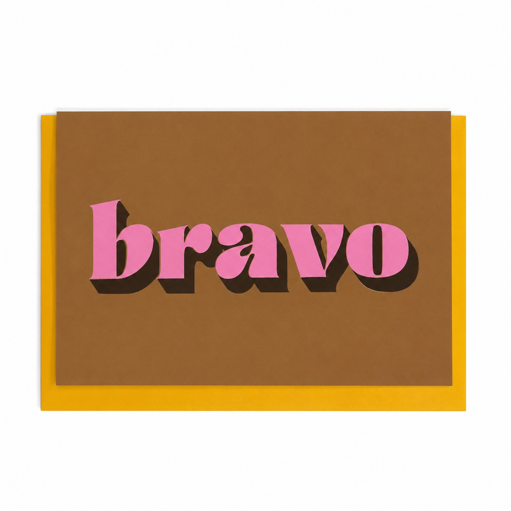 Ochre Bravo card with pink lettering and gold foil detail, shown with a mustard yellow envelope.
