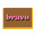 Ochre Bravo card with pink lettering and gold foil detail, shown with a mustard yellow envelope.
