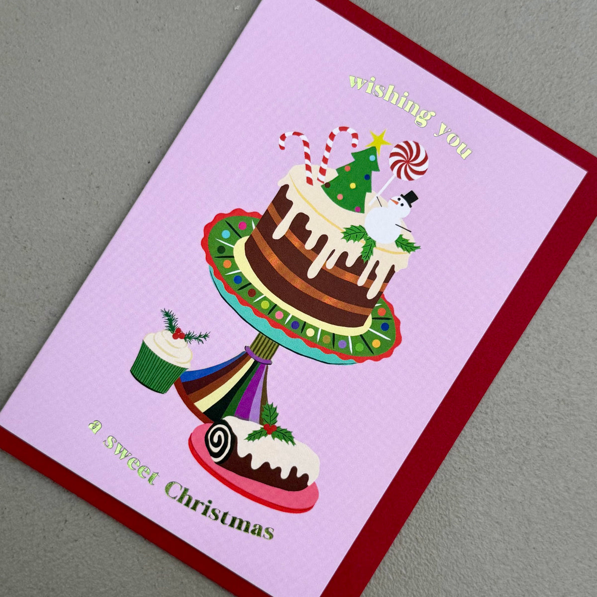 Angled view of Cake Christmas card by PAVILION with festive cake illustration and red envelope

