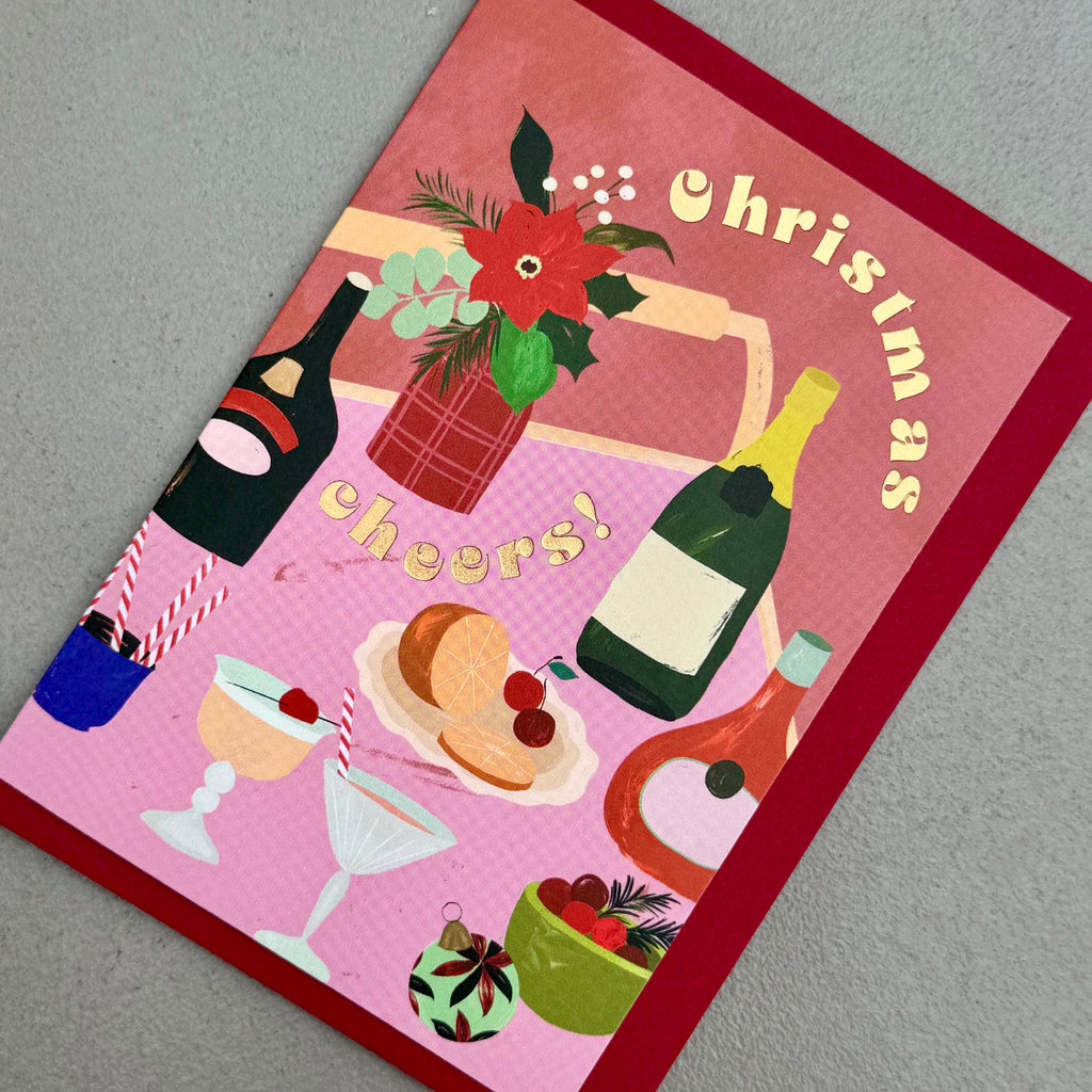 Angled view of Christmas Cheers card by PAVILION with illustrated festive drinks and red envelop