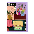 Greeting card featuring an illustrated creative workspace with plants, flowers and stationery on a lilac envelope.