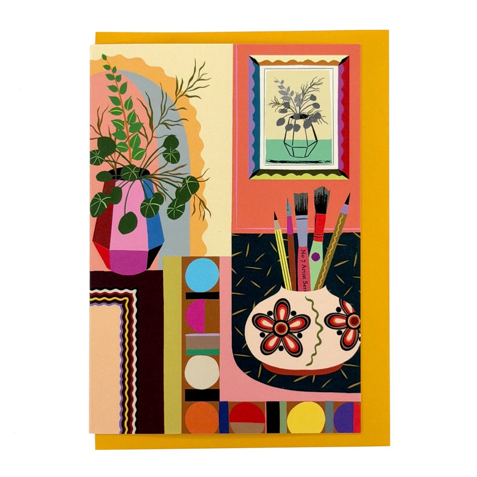 Greeting card featuring an illustrated creative interior with plants, artwork and paintbrushes on a mustard envelope.