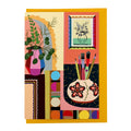 Greeting card featuring an illustrated creative interior with plants, artwork and paintbrushes on a mustard envelope.