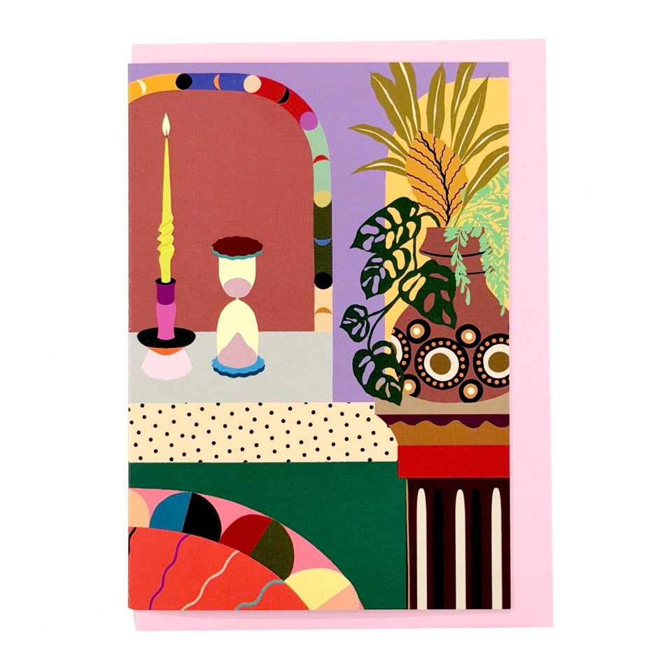 Greeting card featuring an illustrated decorative interior with a candle, hourglass and houseplants on a pink envelope.