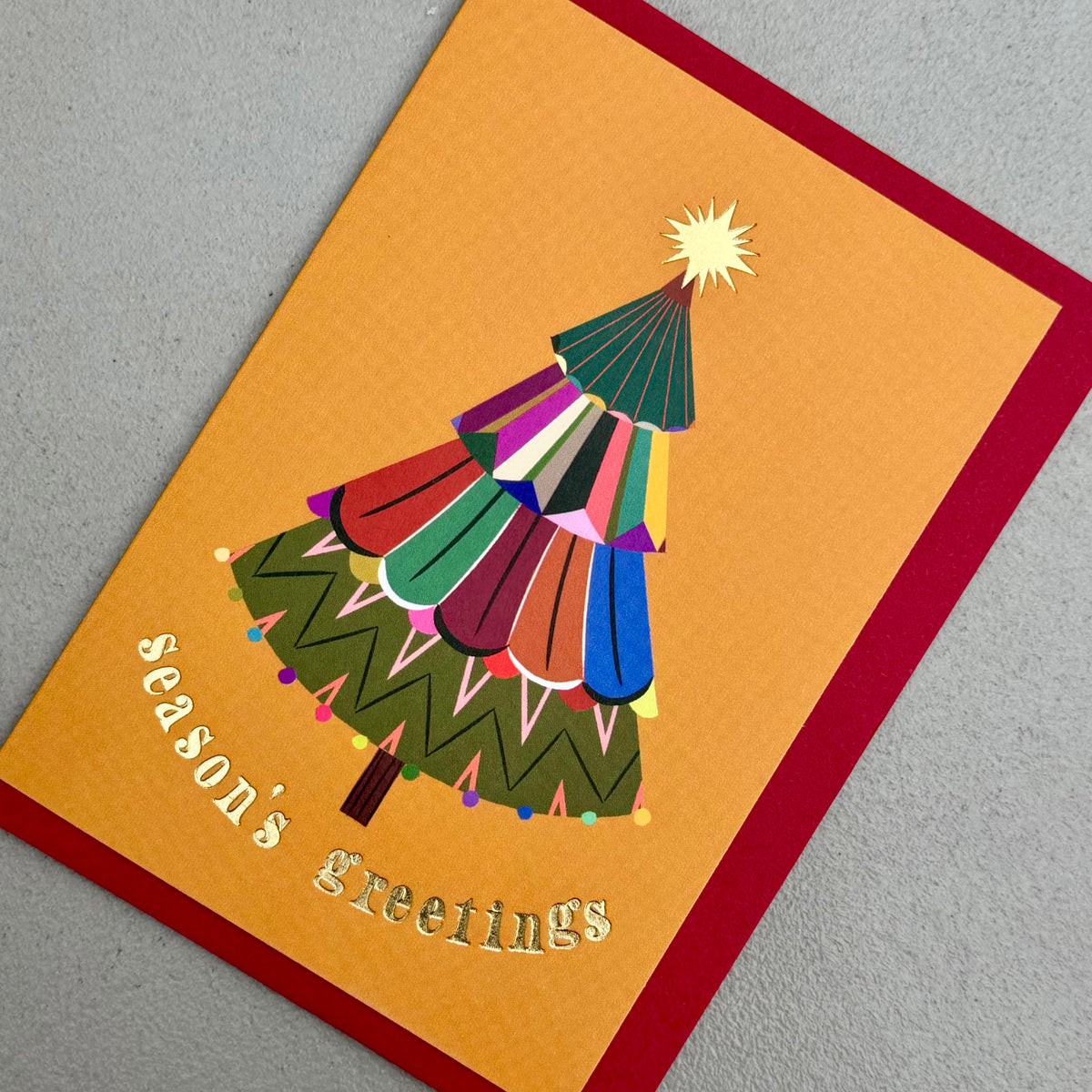 Angled view of Festive Tree Season's Greetings card by PAVILION with red envelope
