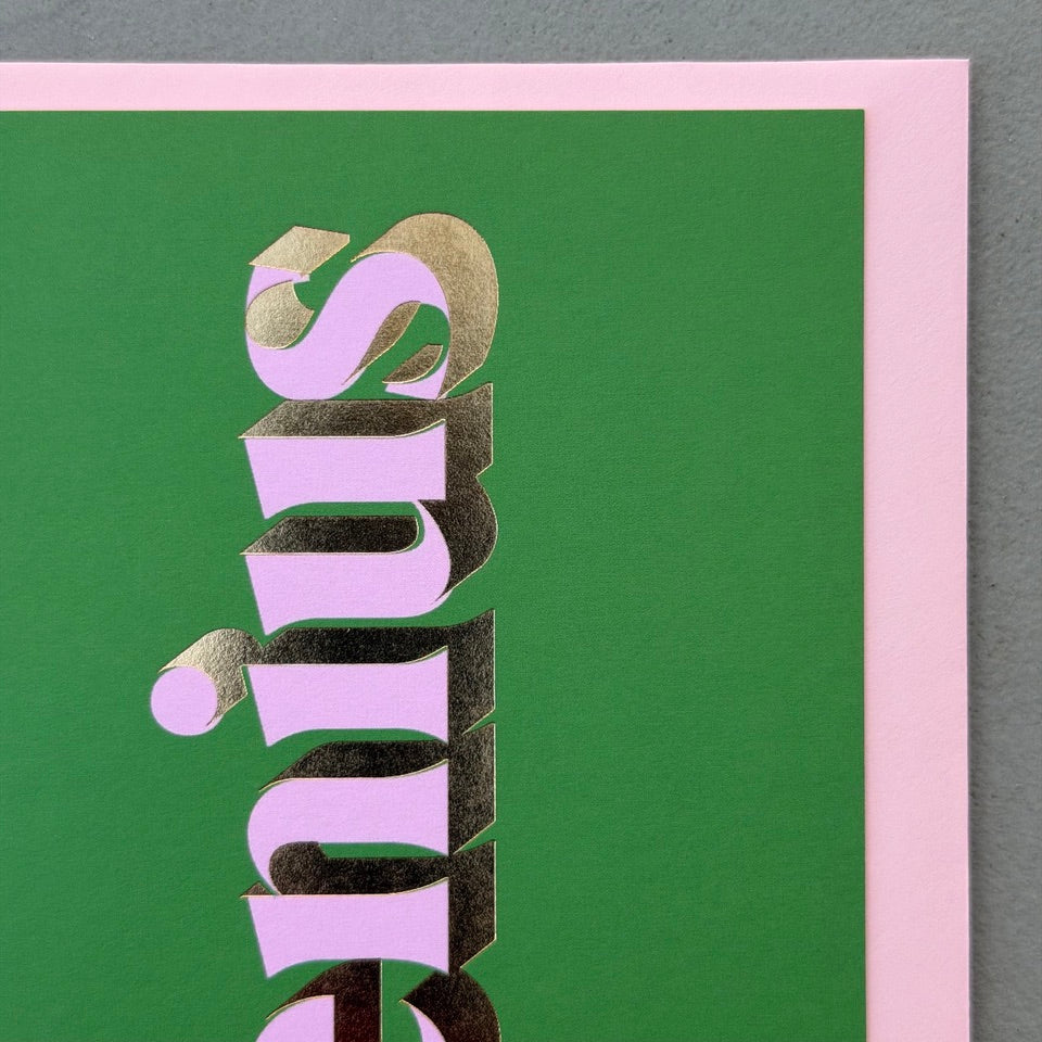 Angled view of the green Genius card showing the lilac lettering and reflective gold foil.
