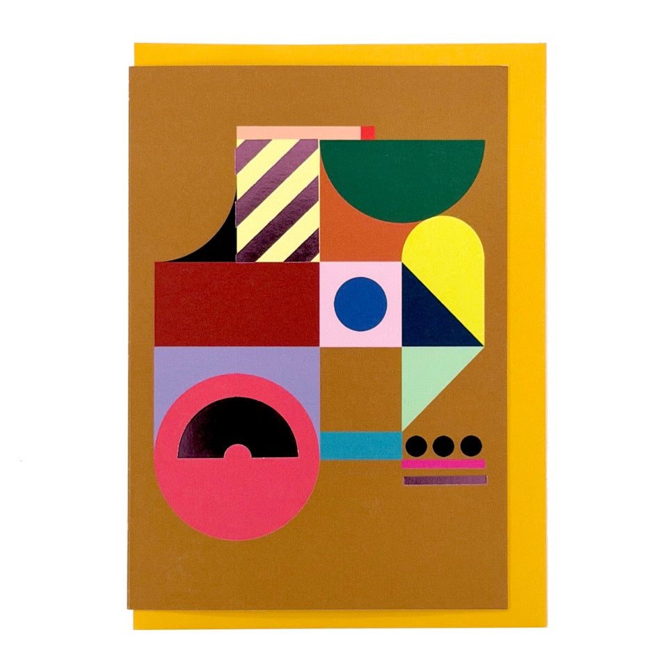 Modern abstract geometric greeting card featuring bold colourful shapes with purple foil details on a warm ochre background, paired with a mustard yellow envelope.