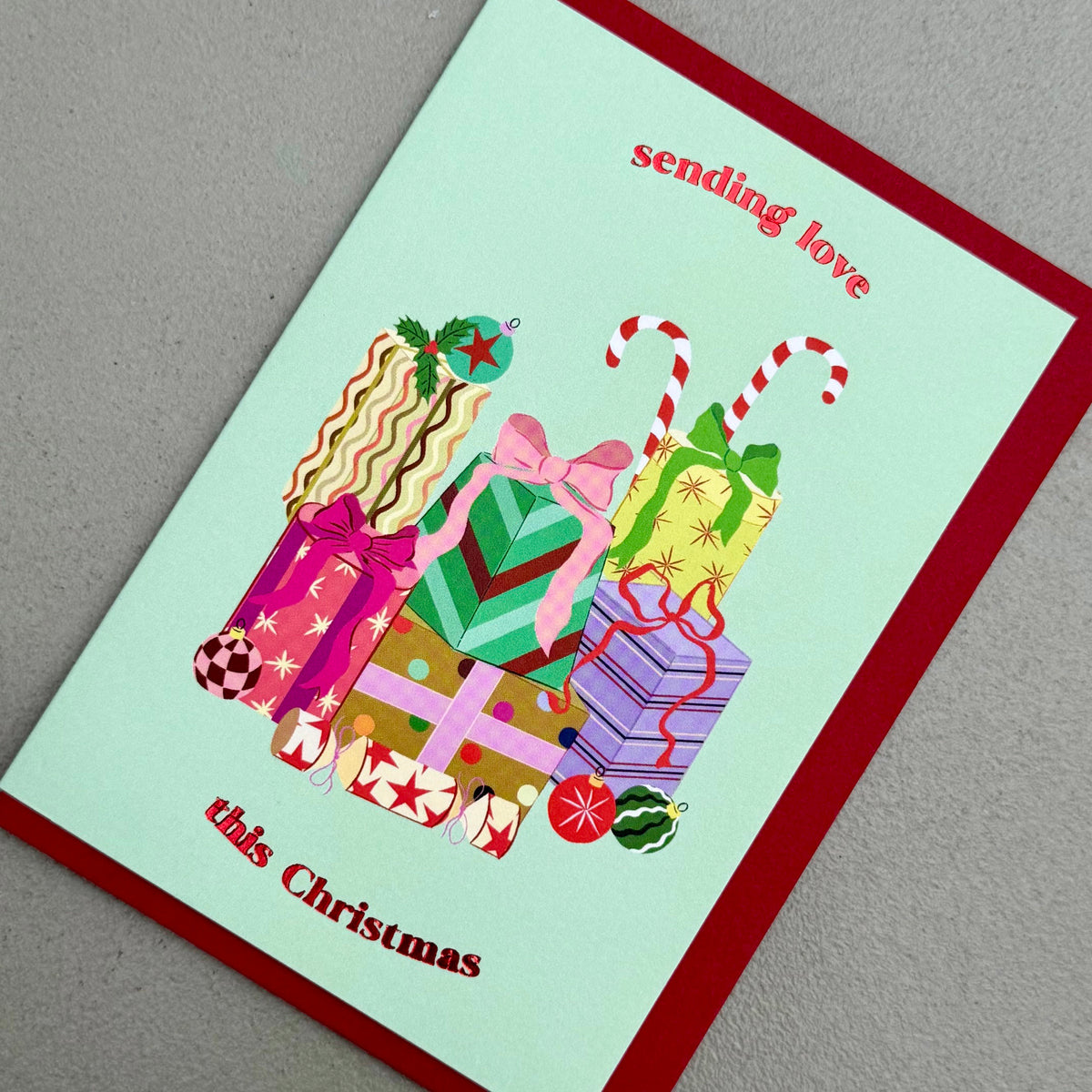 Angled view of Gifts Christmas card by PAVILION with colourful wrapped presents and red envelope

