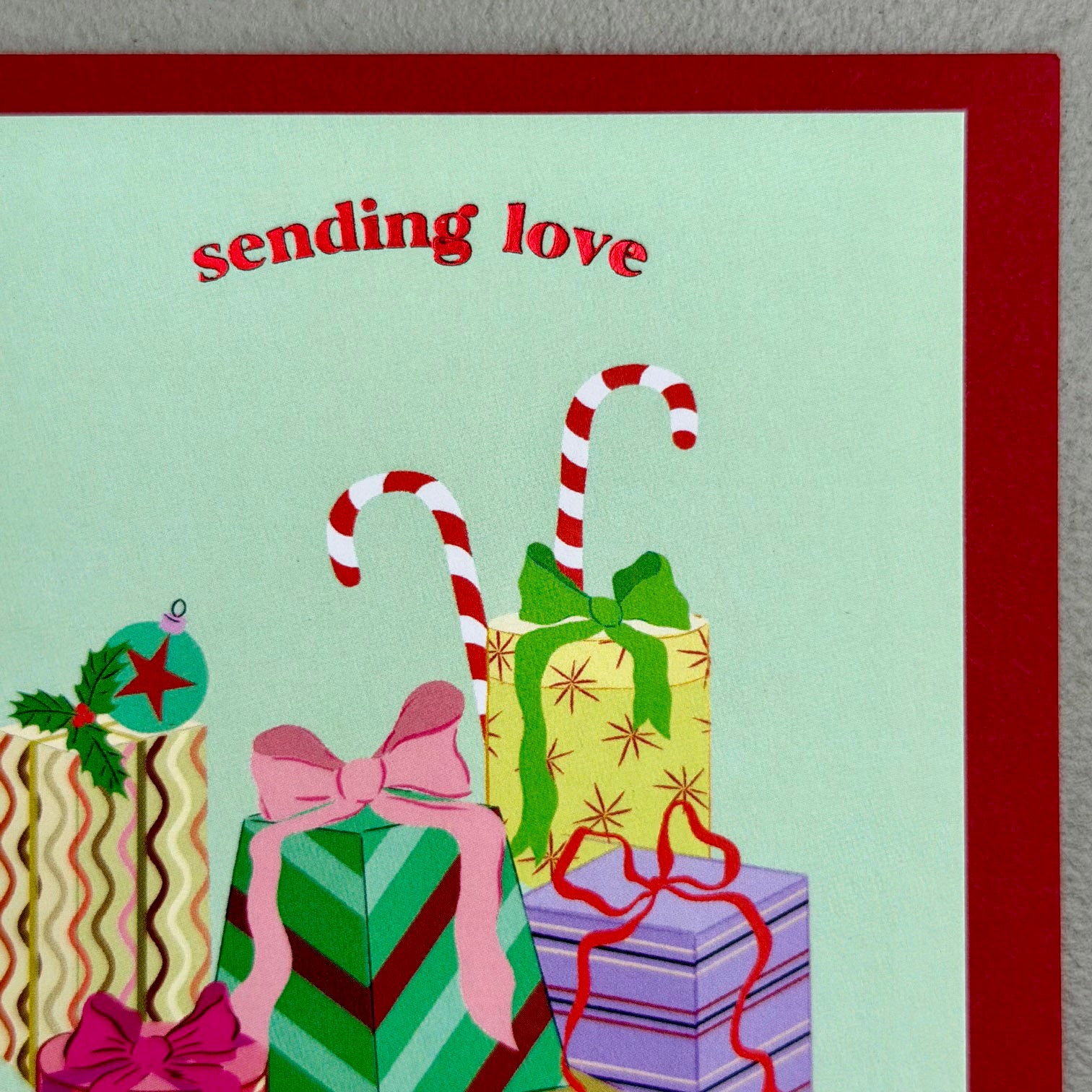Close-up of Gifts Christmas card showing wrapped presents, candy canes and foil “sending love” text
