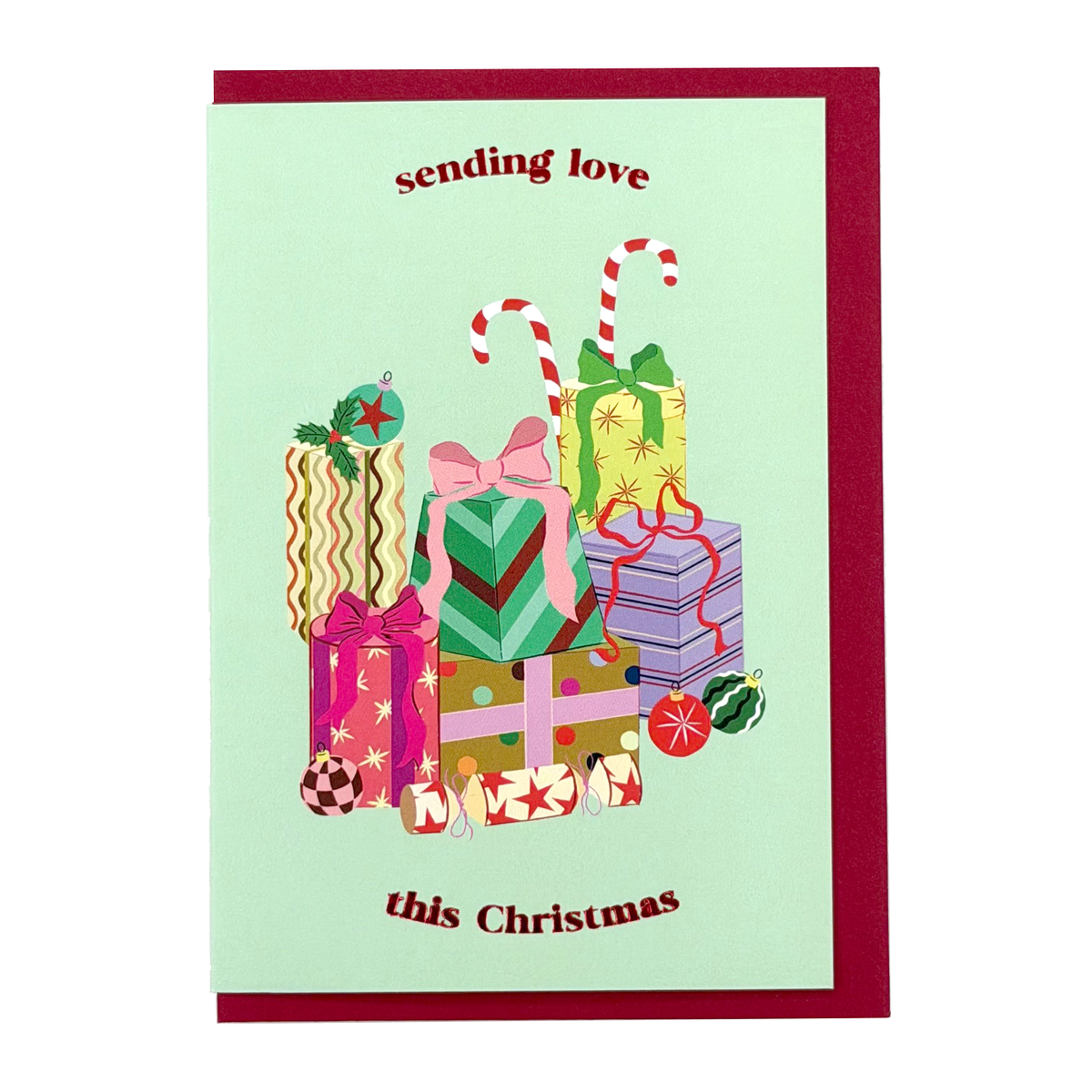 Gifts Christmas card by PAVILION with stacked wrapped presents, candy canes, baubles and the message “sending love this Christmas”