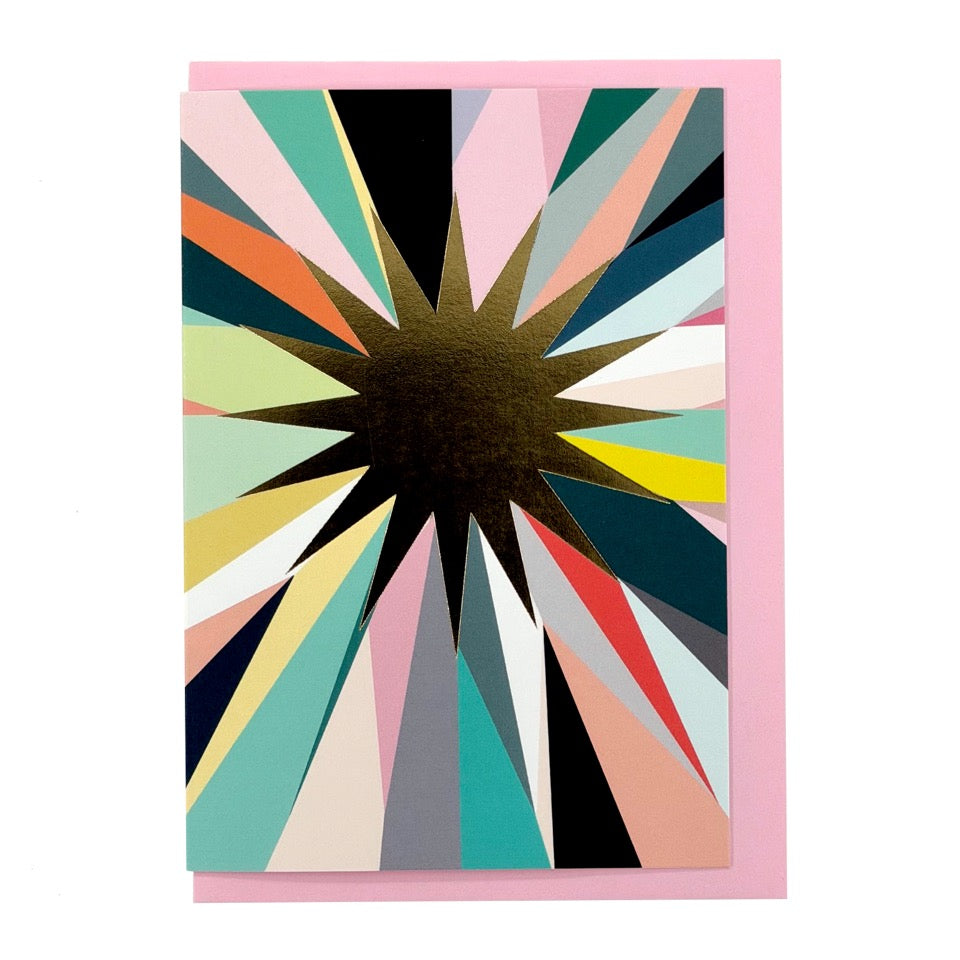 Greeting card featuring a gold foil starburst with soft pastel and jewel-toned rays on a pale pink envelope.