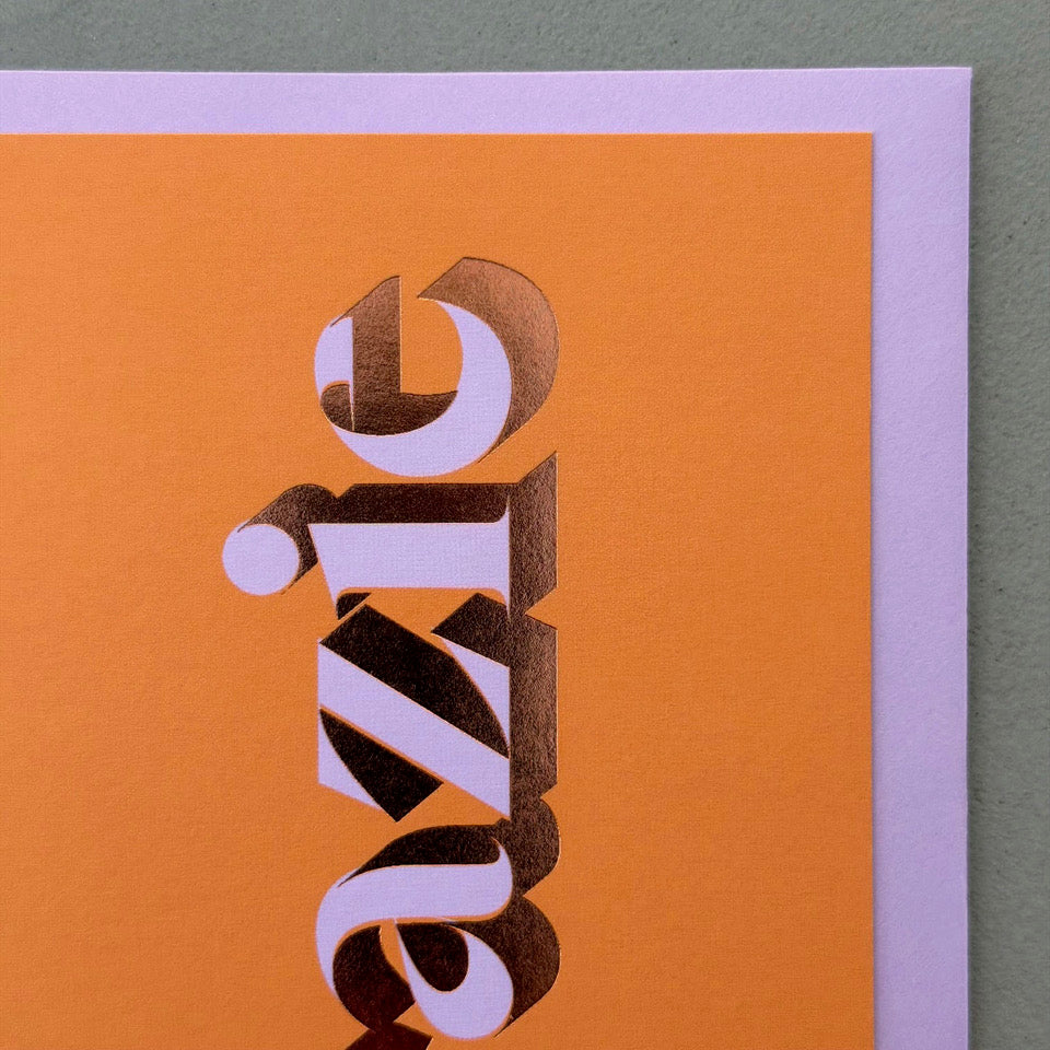 Close-up of the lilac lettering and copper foil detail on the orange Grazie card.
