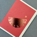 Angled view of the coral pink Happy Birthday card showing the embossed lettering and reflective copper foil.