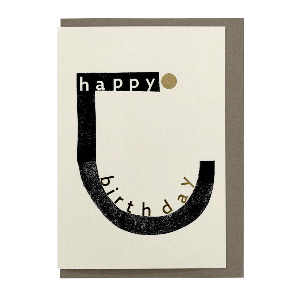 Minimalist Happy Birthday card featuring bold black typography, gold foil accents and a contemporary graphic design, paired with a warm grey envelope.
