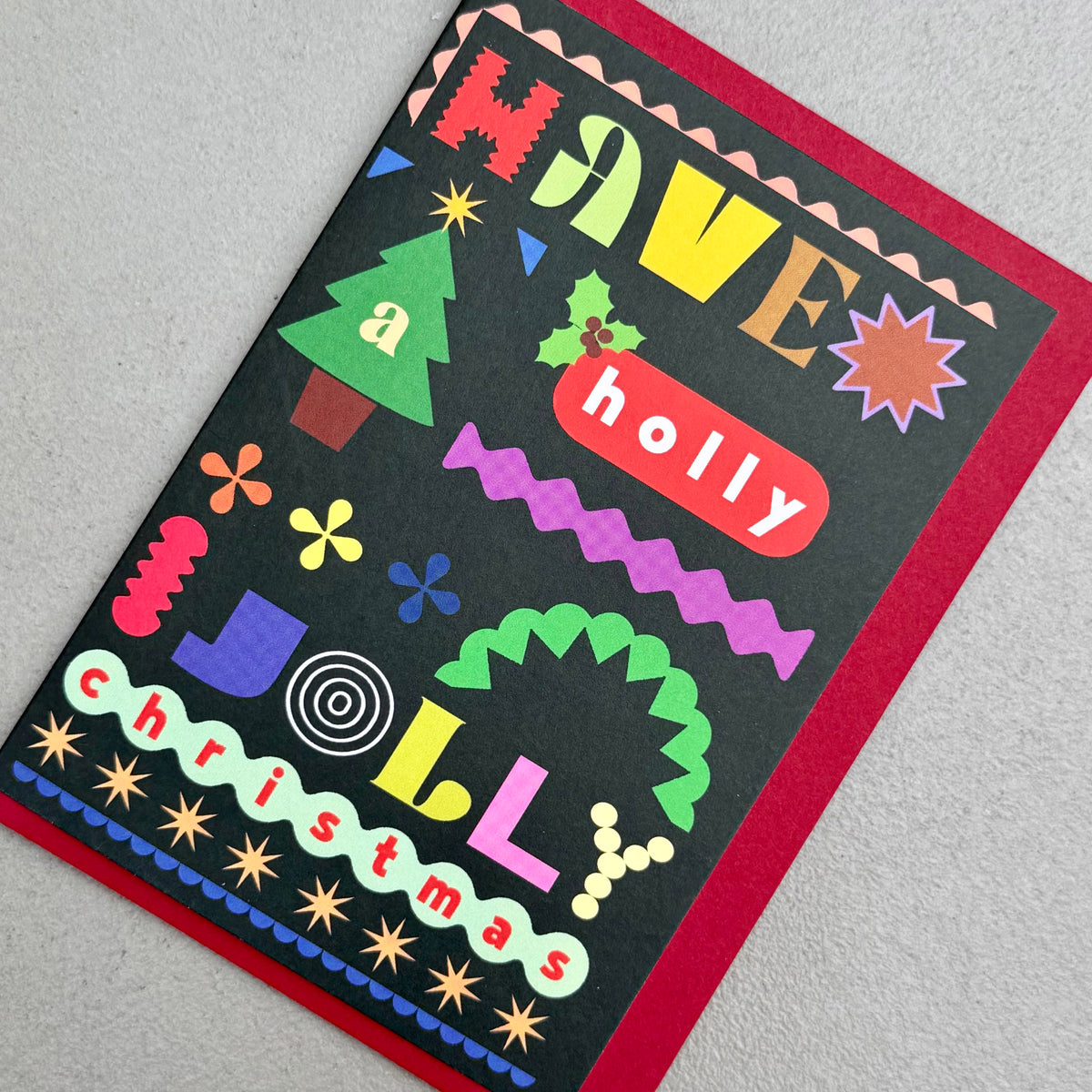 Angled view of Have A Holly Jolly Christmas card by PAVILION with red envelope