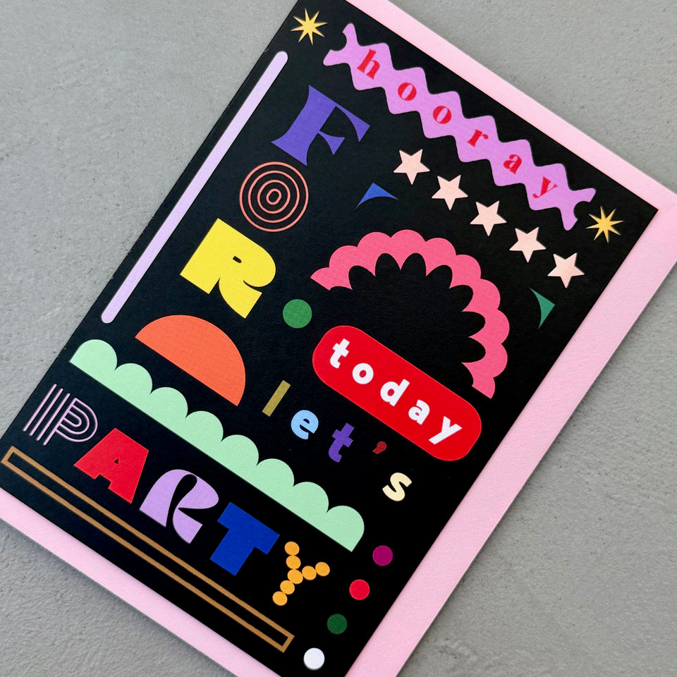 Angled view of the Hooray For Today Let's Party greeting card on a pale pink envelope.
