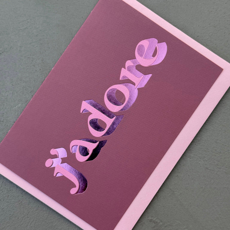 Angled view of the mauve J’adore card showing the pink lettering and reflective pink foil.
