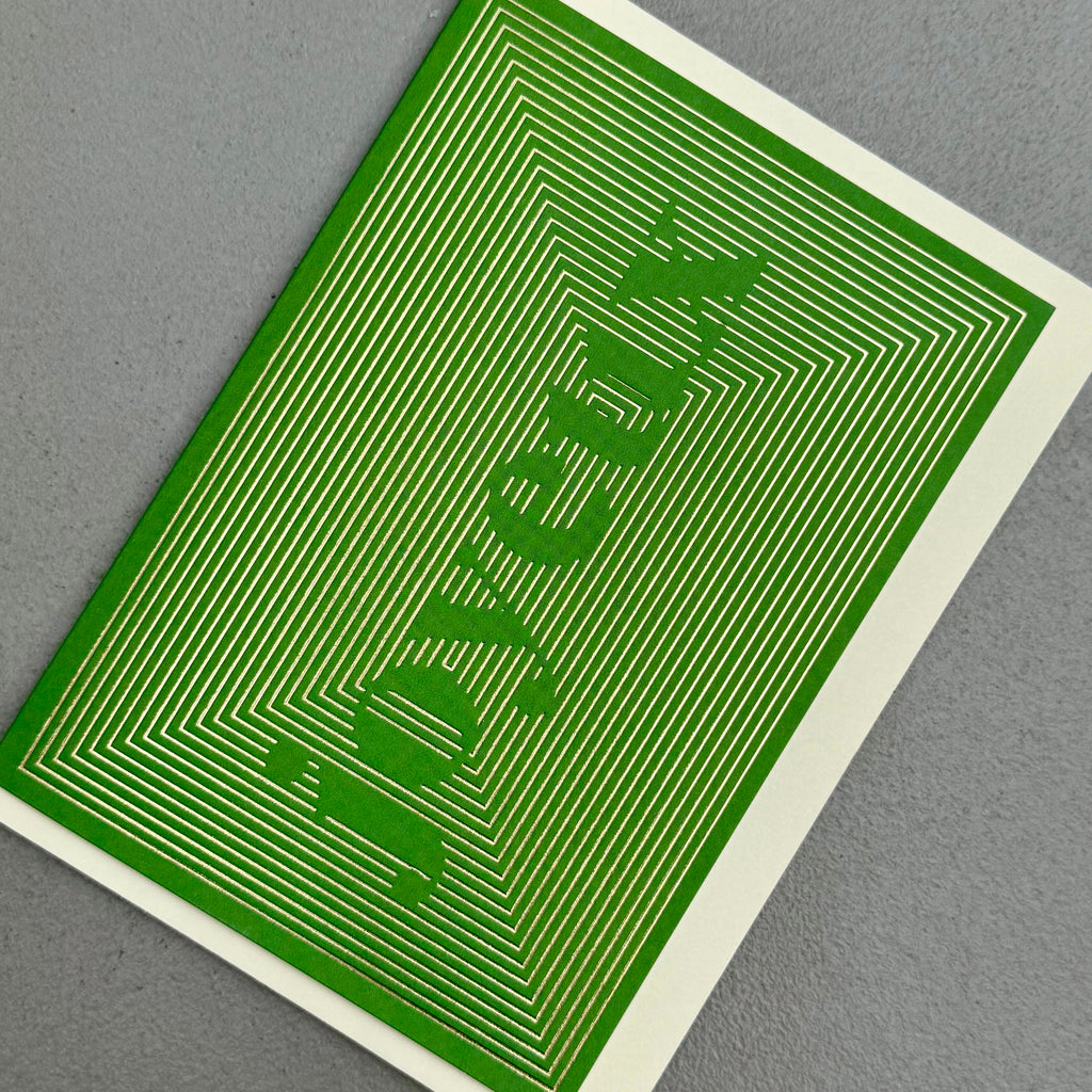 Angled view of Joyeux Christmas card by PAVILION with gold foil linework forming the word Joyeux on a green background
