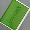 Angled view of Joyeux Christmas card by PAVILION with gold foil linework forming the word Joyeux on a green background

