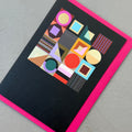Angled view of the Modern Geometric greeting card with a bright pink envelope, showcasing the abstract geometric artwork and gold foil details.