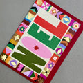 Angled view of NOEL Christmas card by PAVILION with graphic lettering, decorative border and red envelope
