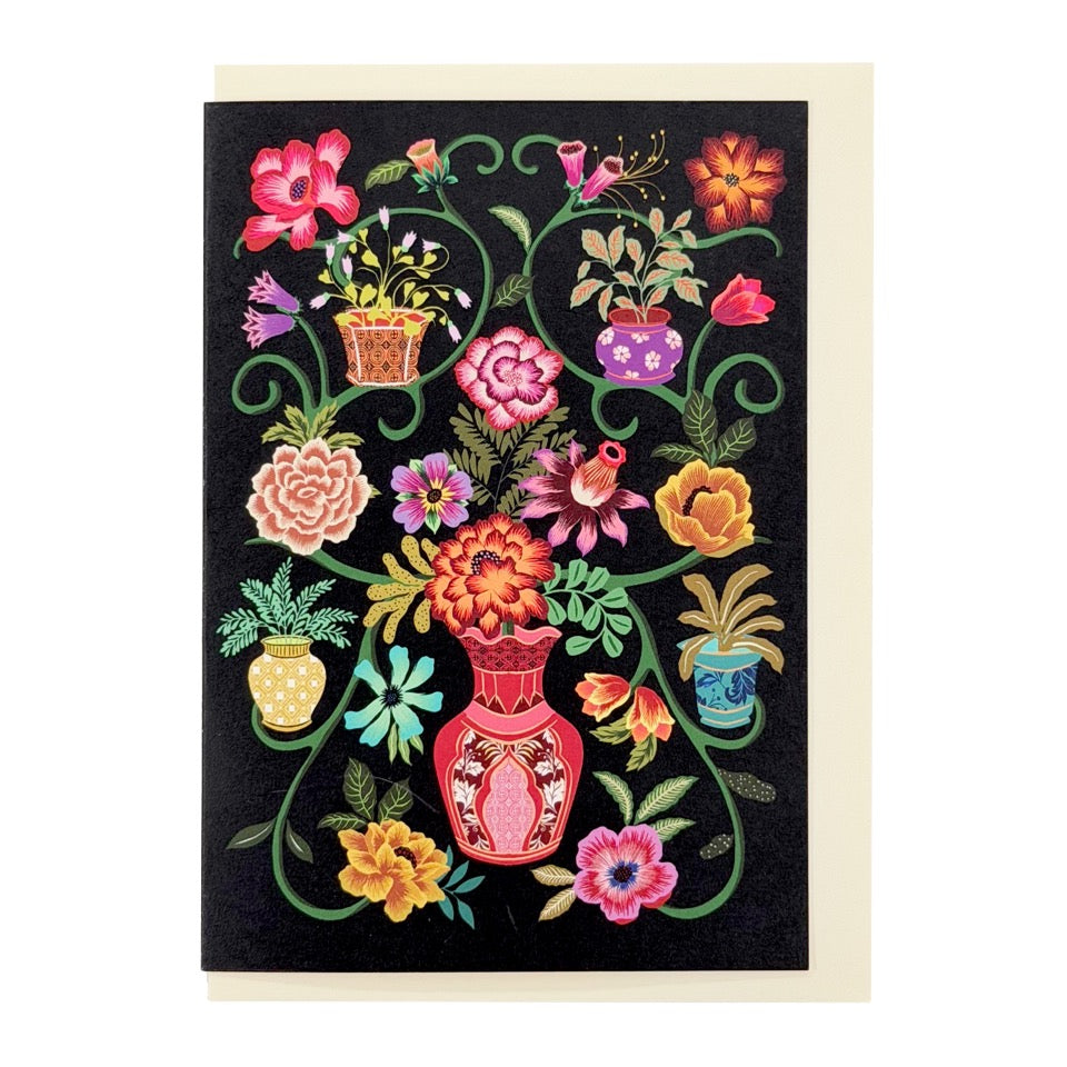 Illustrated floral greeting card featuring colourful flowers, decorative vases and winding green stems on a black background, paired with a cream envelope.