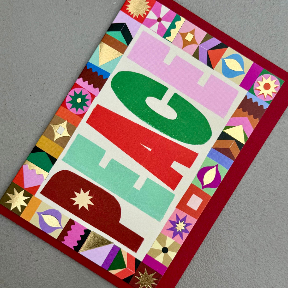 Angled view of PEACE Christmas card by PAVILION with graphic lettering, decorative border and red envelope
