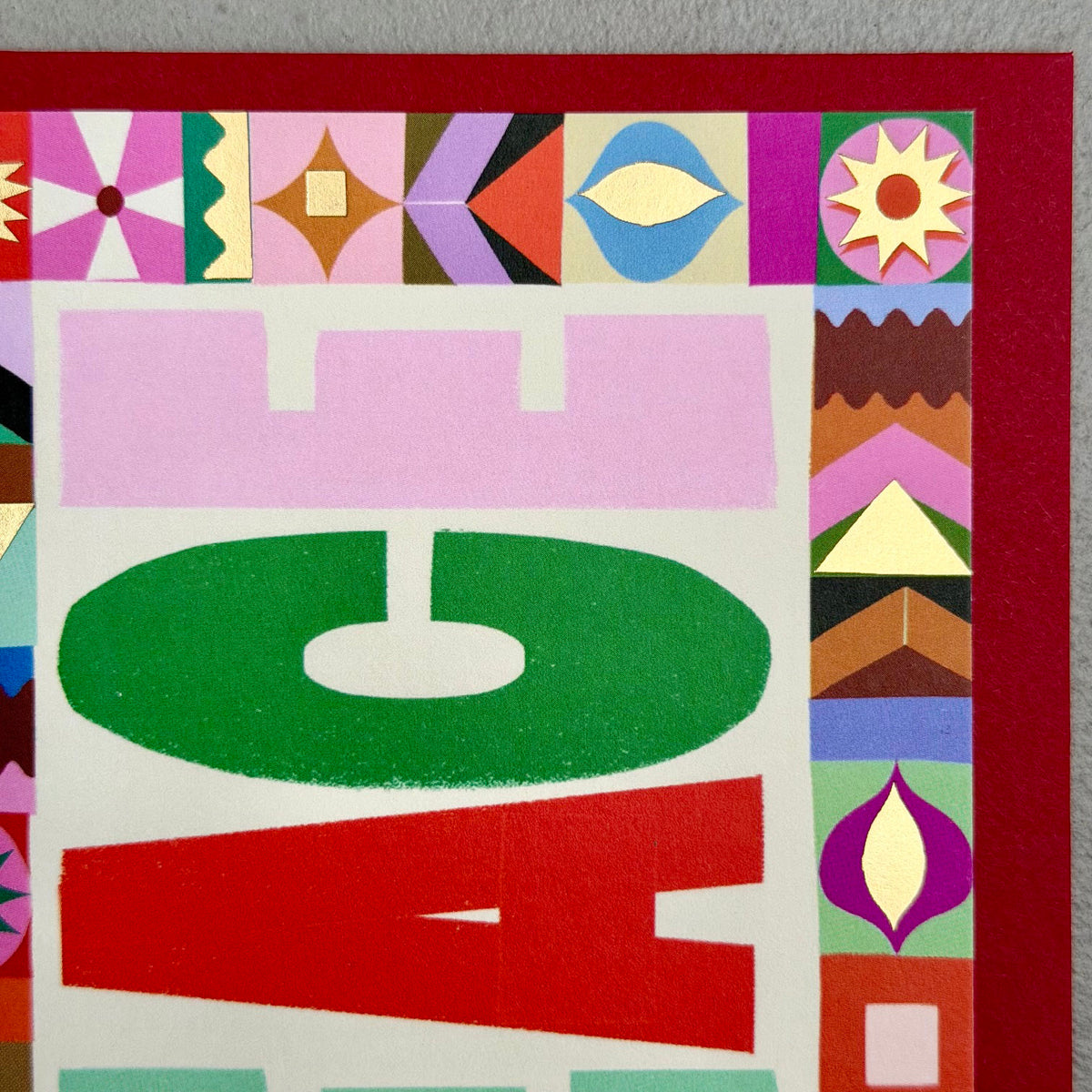 Close-up of PEACE Christmas card showing bold letterforms, patterned border and gold foil details
