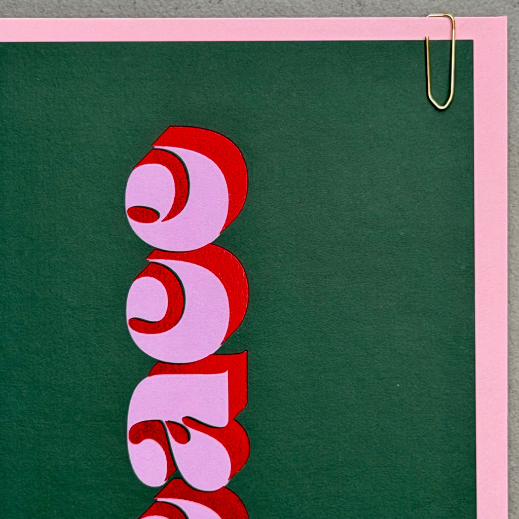 Detail of the Peace Christmas card showing red foil lettering and gold paperclip