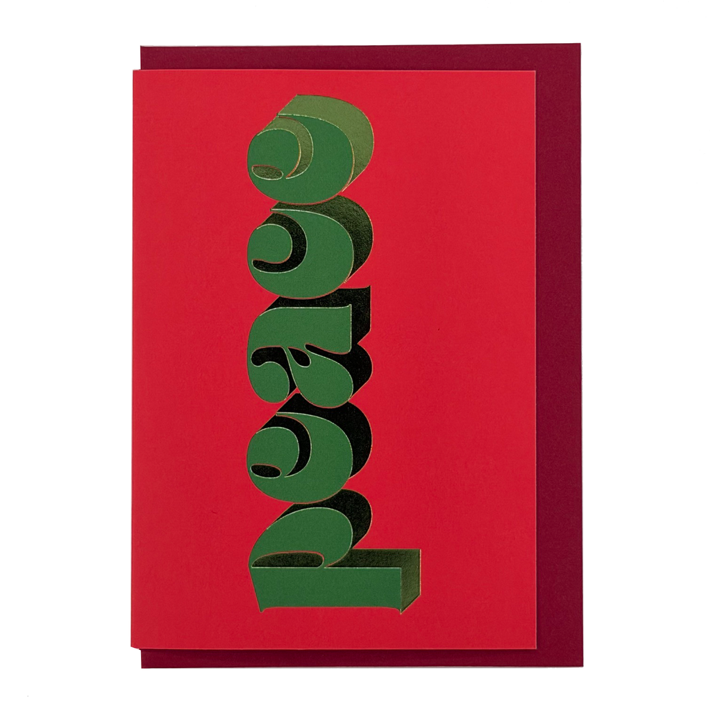 Front view of Peace Christmas card by PAVILION with green sculptural lettering on a vivid red background and red envelope