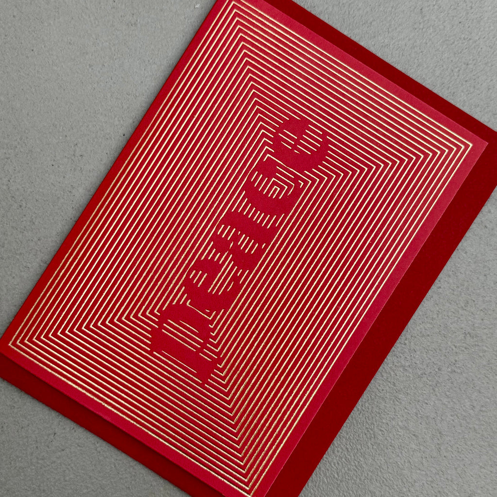 Angled view of Peace Christmas card by PAVILION with gold foil linework forming the word Peace on a red background