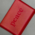 Angled view of Peace Christmas card by PAVILION with gold foil linework forming the word Peace on a red background