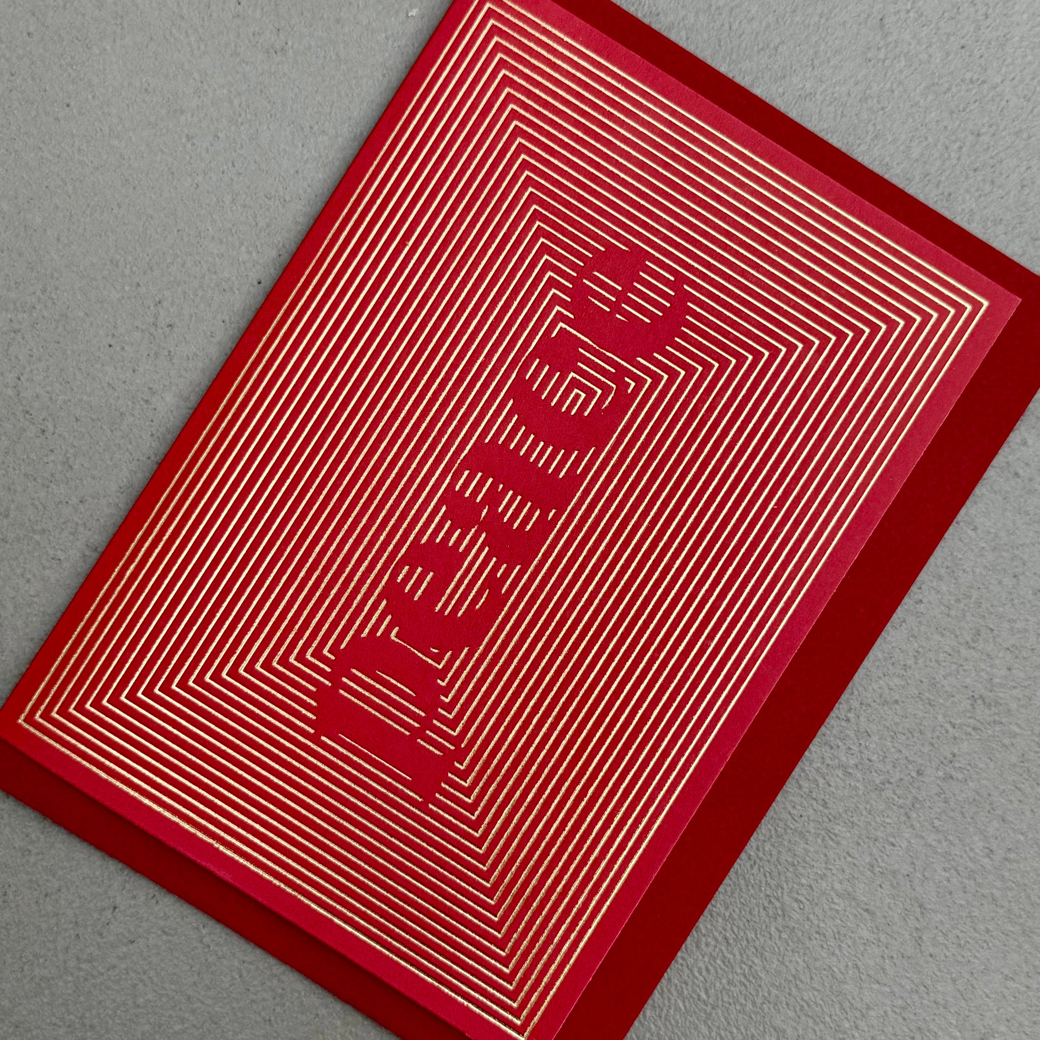 Angled view of Peace Christmas card by PAVILION with gold foil linework forming the word Peace on a red background