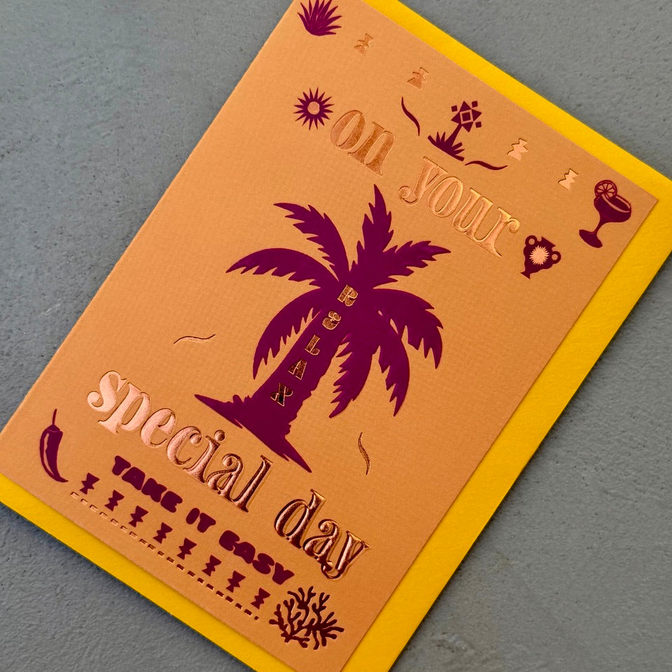 Angled view of the Relax On Your Special Day greeting card with a bright yellow envelope, showcasing the bold tropical design and foil details.
