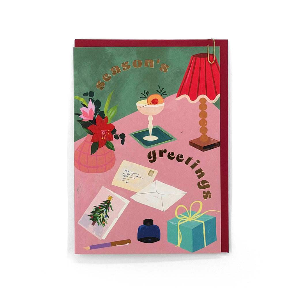 Season's Greetings Christmas card featuring a festive tabletop scene with gold foil lettering