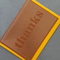 Angled view of the Thanks Gold Foil greeting card with a mustard yellow envelope, showcasing the bold geometric line pattern and metallic gold foil finish.