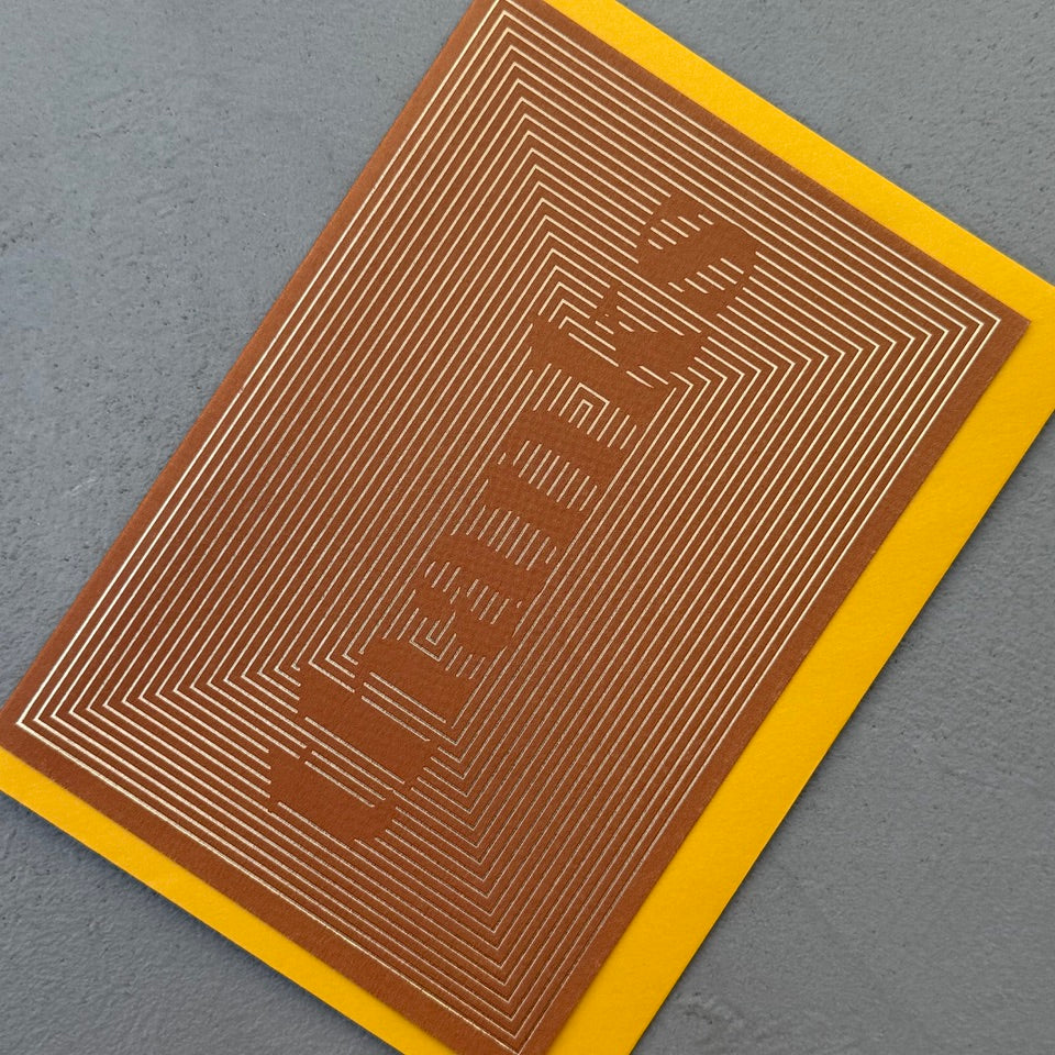 Angled view of the Thanks Gold Foil greeting card with a mustard yellow envelope, showcasing the bold geometric line pattern and metallic gold foil finish.