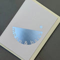 Angled view of the pale grey To the Moon & Back card showing the embossed lettering and reflective silver foil.
