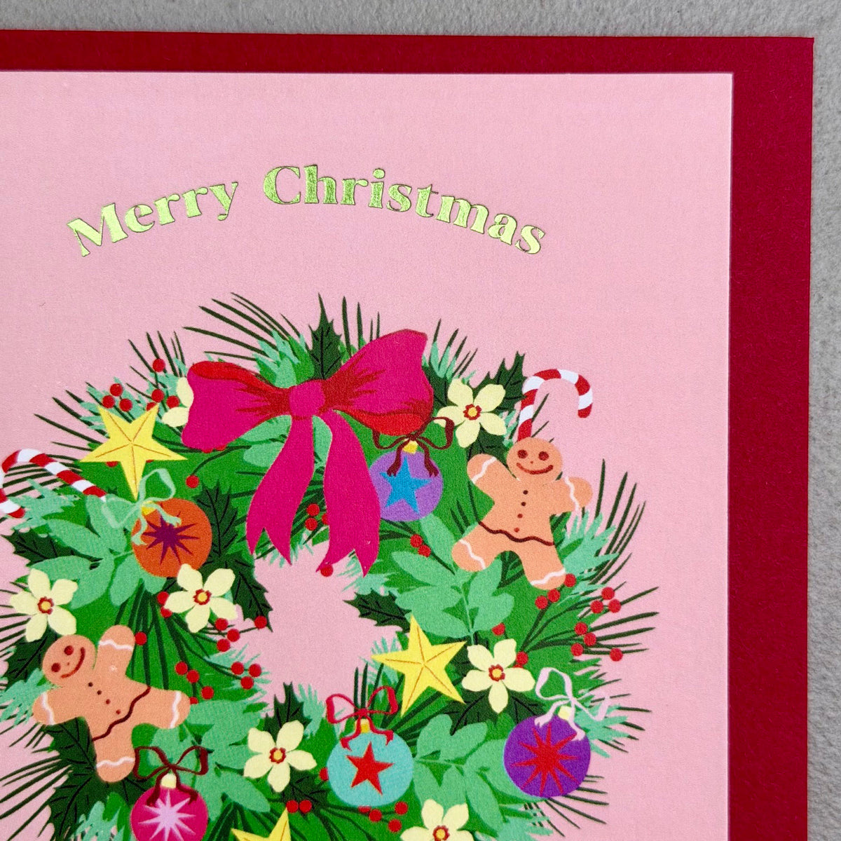 Close-up of Wreath Christmas card showing festive foliage, gingerbread men, ornaments and foil lettering
