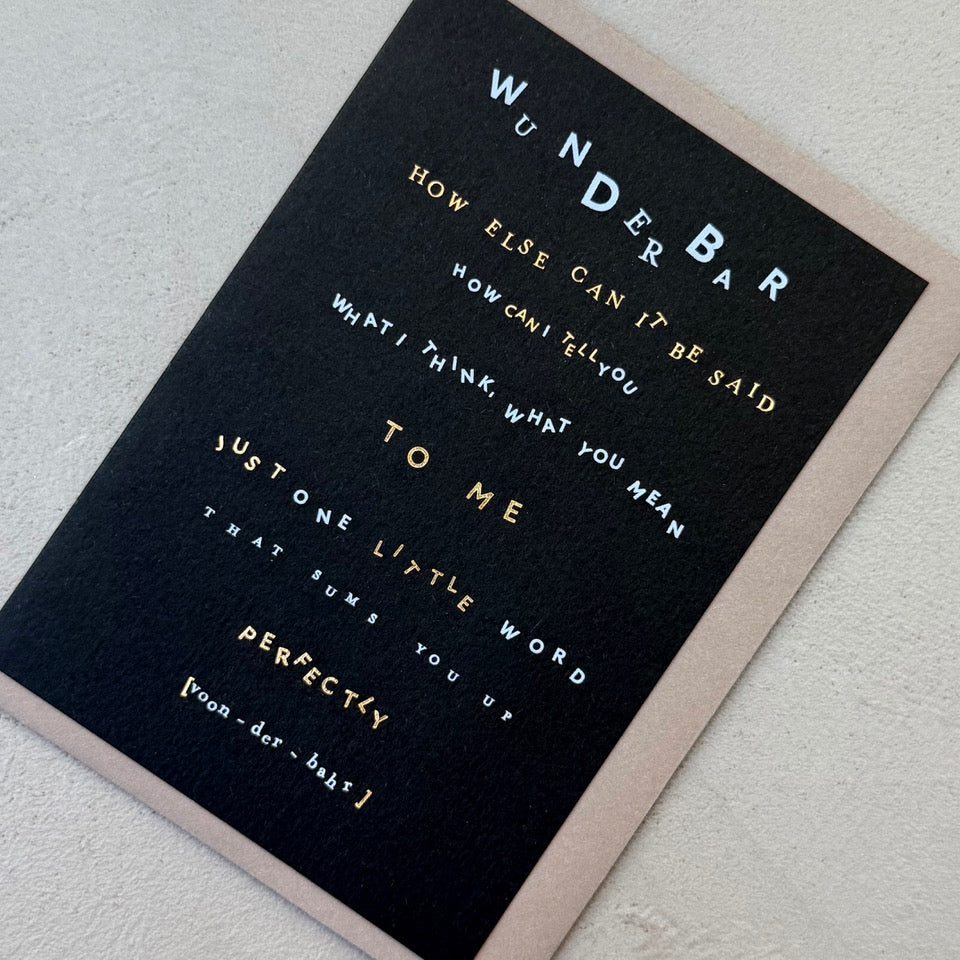 Angled view of the Wunderbar Typography greeting card with a mink envelope, showcasing the contemporary typographic layout and gold foil details.