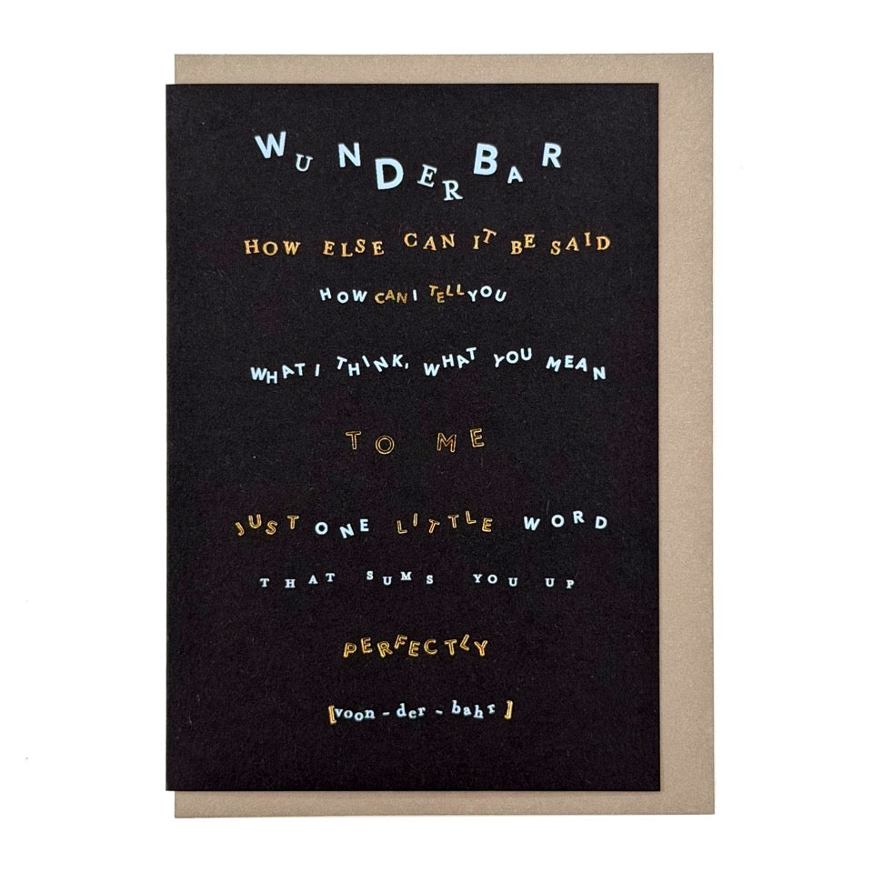 Contemporary typography greeting card featuring the word "Wunderbar" with playful lettering and gold foil details on a black background, paired with a stone-grey envelope.
