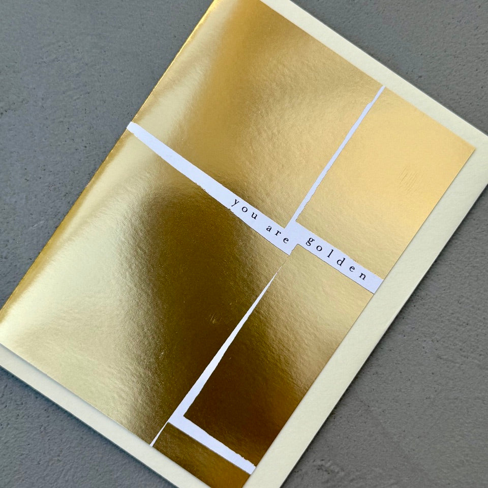 Angled view of the You Are Golden greeting card with a cream envelope, showcasing the striking full gold foil design and modern minimalist style.