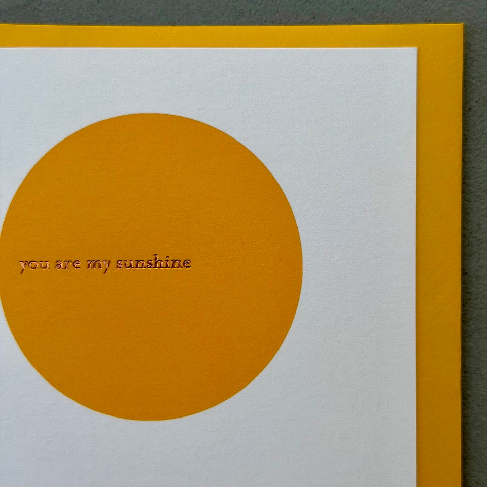 Close-up of the You Are My Sunshine greeting card highlighting the warm golden circle, subtle gold foil lettering and textured white card stock.